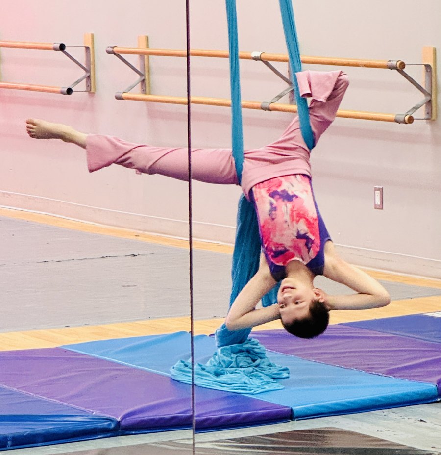 Belle hanging upside down on aerial silks, smiling