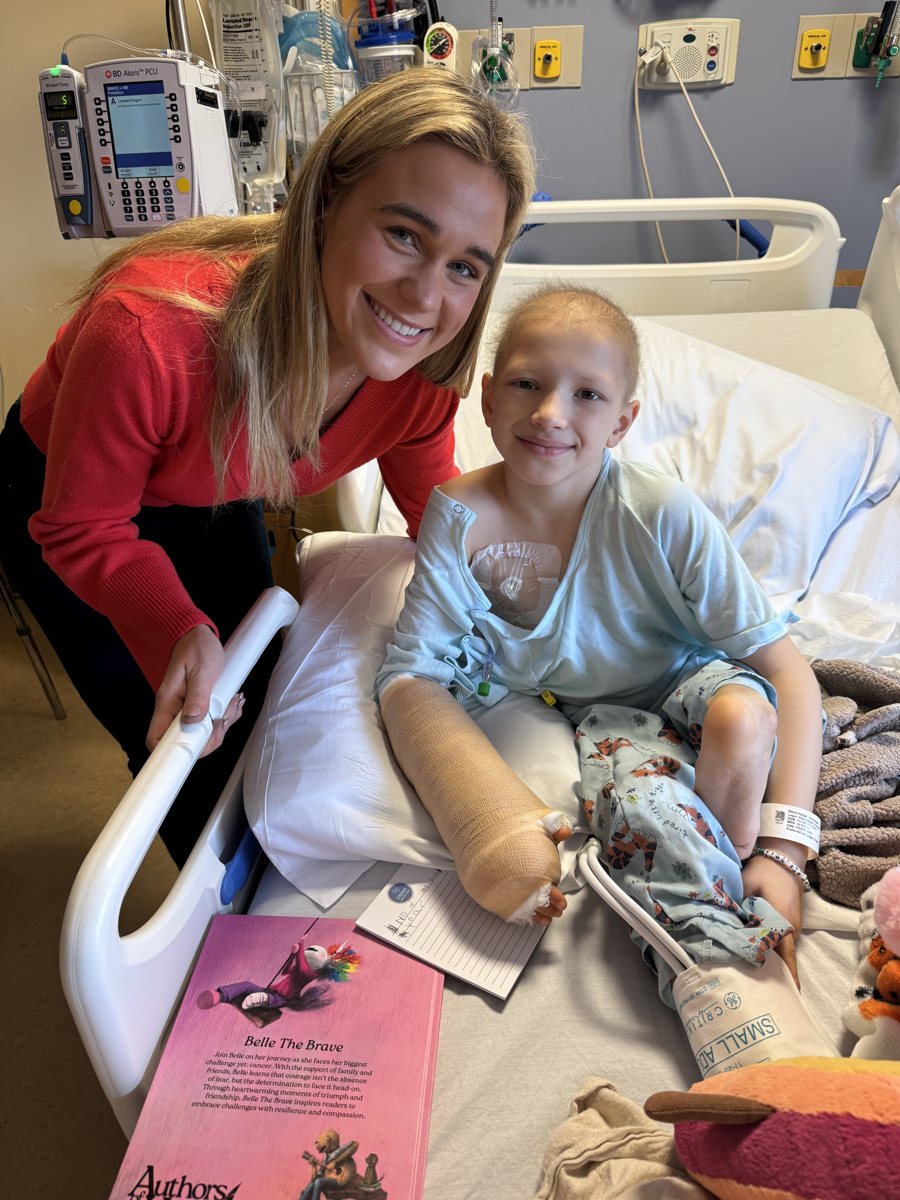 Belle in her hospital bed after surgery, holding up a copy of her book