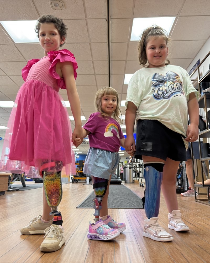 Belle holding hands with two younger girls who also wear prosthetic legs