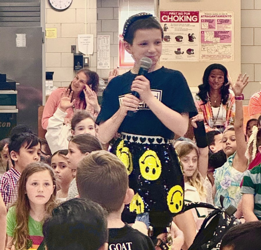 Belle speaking with a microphone to a school assembly